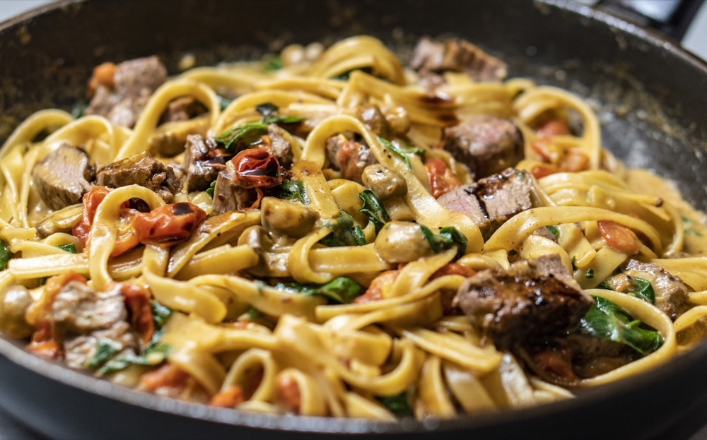 Bandnudeln mit Fleisch und Kräutern in der Pfanne